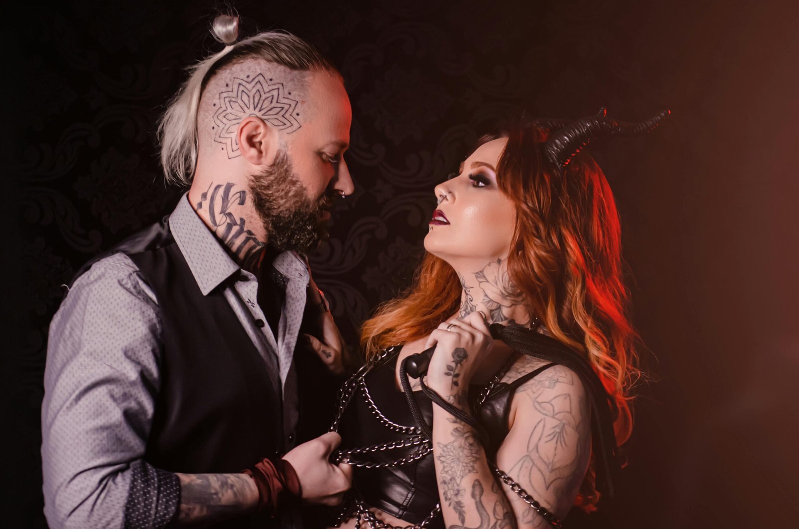 A striking portrait of a tattooed couple in edgy costumes with dramatic lighting.