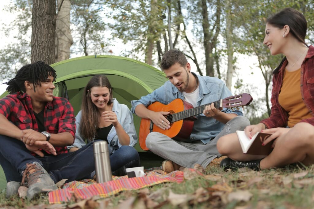 Young friends camping and enjoying music together in a tranquil outdoor setting.