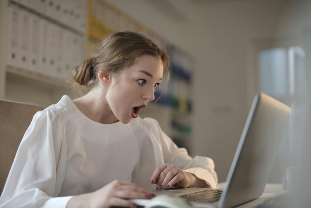 Surprised woman sitting at desk with laptop indoors, expressing amazement.