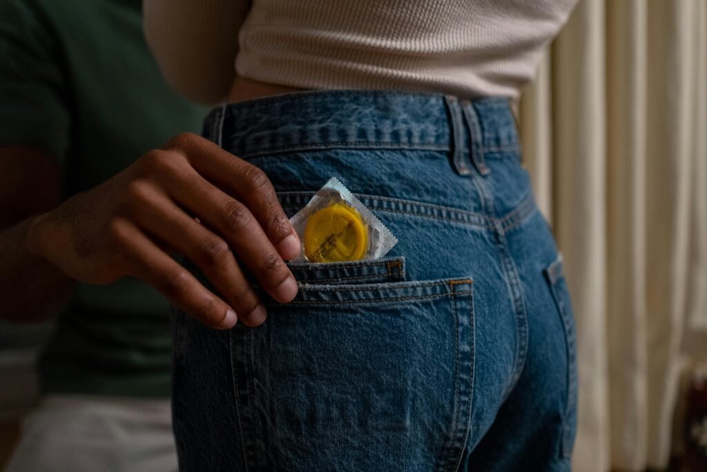 Condom being placed into denim jeans pocket, emphasizing safe sex and contraceptive use.