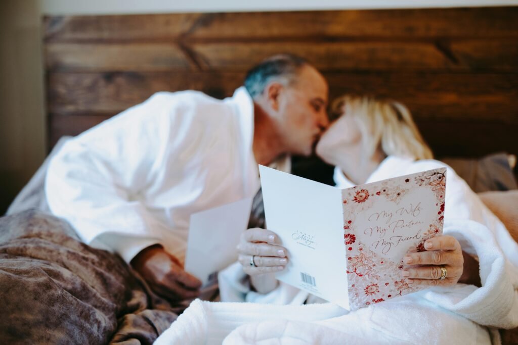 Senior couple shares an intimate moment with a romantic card indoors, showcasing love and companionship.