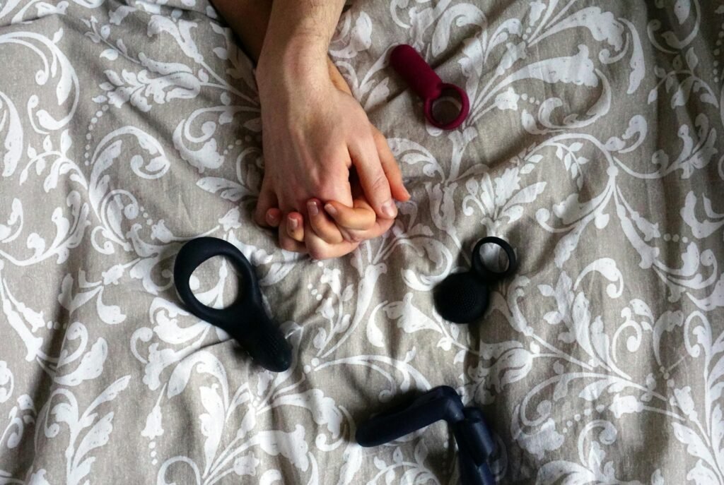 Intimate scene with hands holding on a patterned bedspread with adult toys.